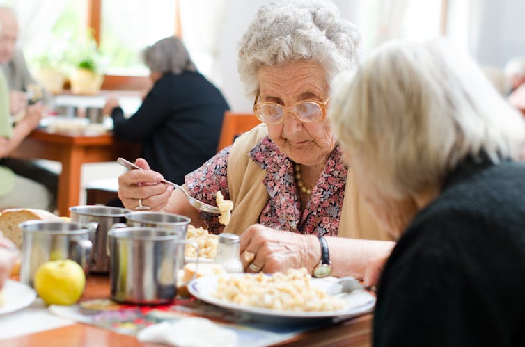 Two senior women eating in an aged care facility.