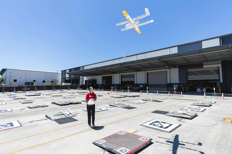 Photo of a woman holding a paper bag to be attached to a hovering drone.