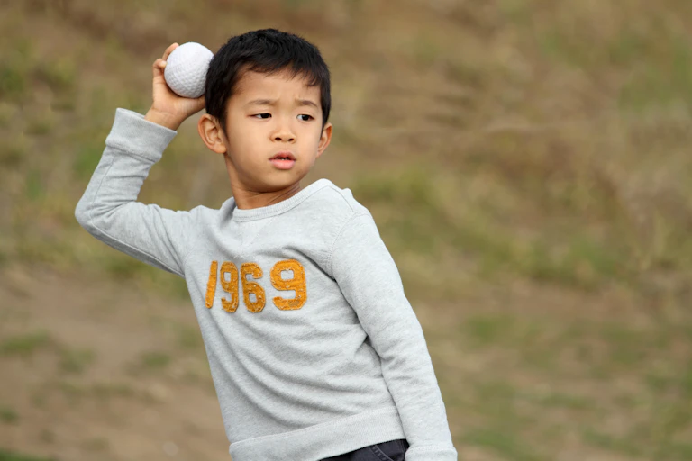 A young boy holds a ball above his head, poised to throw.