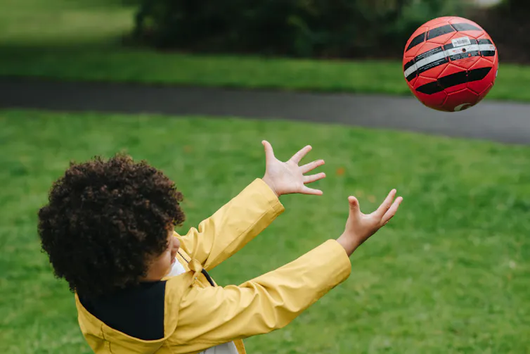 A ball comes towards a child with their arms outstretched.