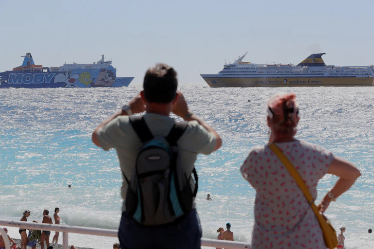 deux personnes de dos regardent des ferrys dans la mer