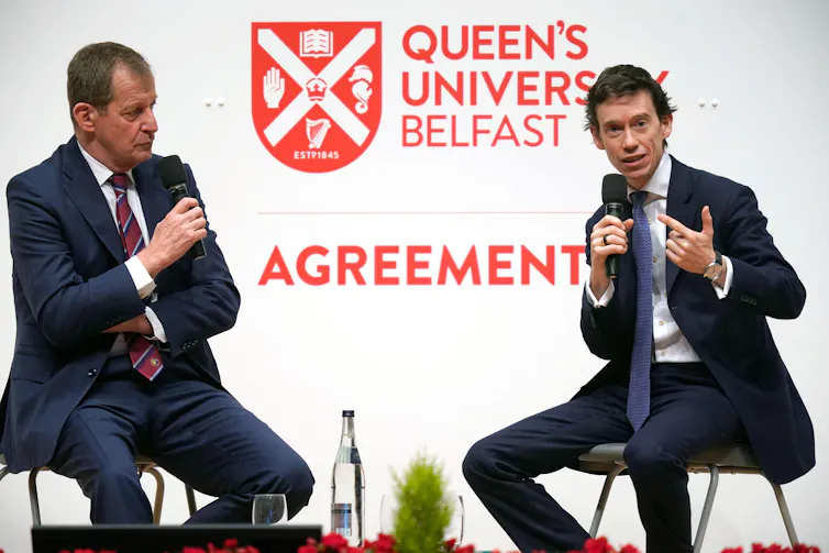 Alastair Campbell and Rory Stewart sitting on chairs on a stage, speaking into microphones at Queen's University Belfast