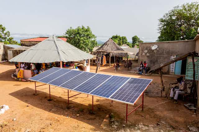 6 large solar panels mounted off the ground surrounded by huts and small houses