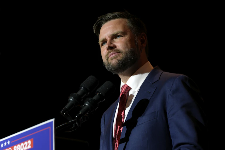 A middle-aged white man stands before a podium with a microphone on it