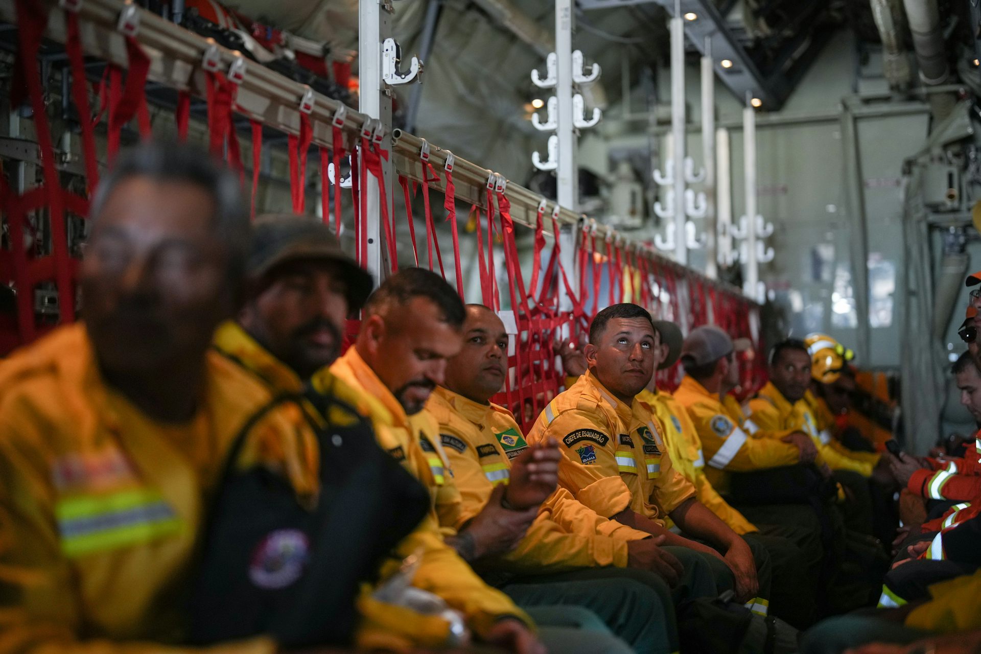 A group of men sit in a row against the fuselage of an airplane.