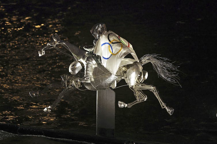 The Horsewoman, draped in the Olympic flag, rides along on the River Seine.