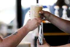 Close up of the hand of a customer taking a to-go coffee cup from the hand of a barista