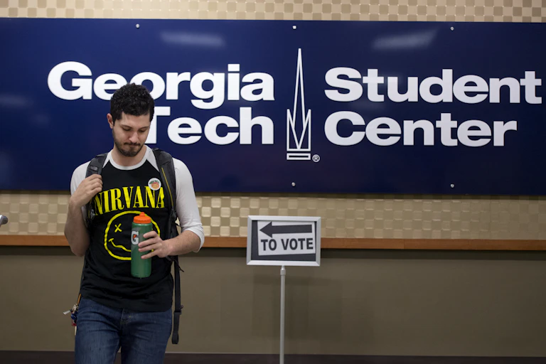 Young man in a Nirvana shirt walks by a voting sign at the Georgia Tech student center.