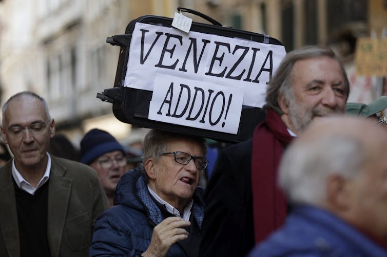 A man holding at a protest carries a sign in italian that reads: Venezia Addio