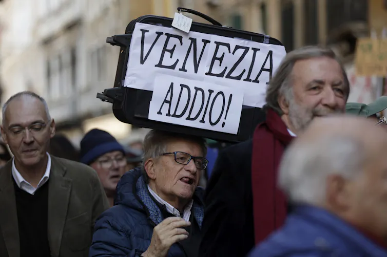 A man holding at a protest carries a sign in italian that reads: Venezia Addio