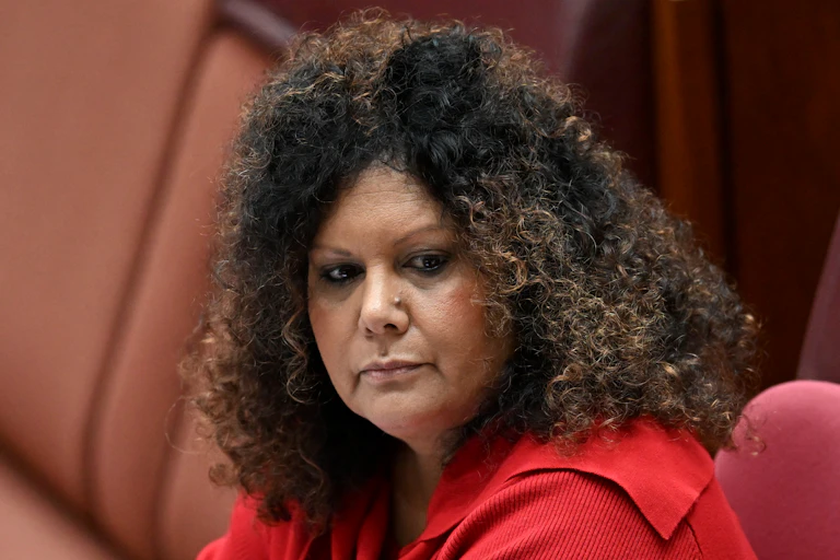 An Indigenous woman in a red top looks to the right