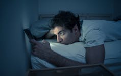 Man in bed reading from screen of mobile phone