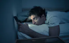 Man in bed reading from screen of mobile phone