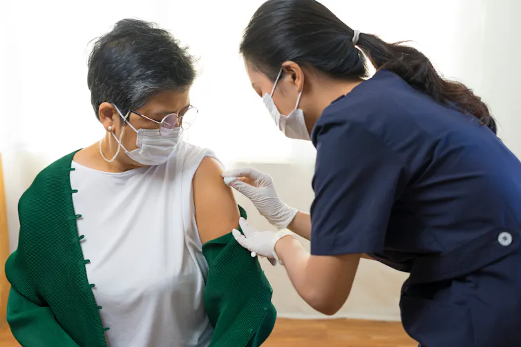 A woman receives a vaccination from a female nurse.