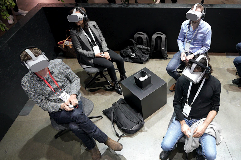 A group of people wearing VR headsets sitting in an empty room.