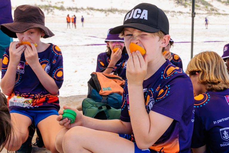 Students eat oranges during a beach football competition