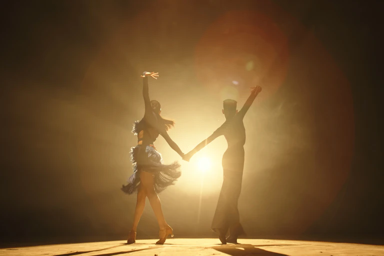 Silhouette of a pair of ballroom dancers striking a pose onstage while a spotlight glows behind them