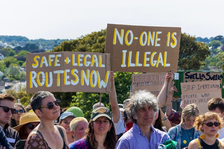 Protesters holding handmade signs reading 'safe and legal routes now' and 'no one is illegal'