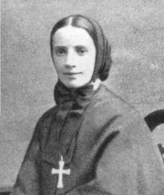 A portrait of a young woman who is wearing a crucifix around a gown with her head covered.