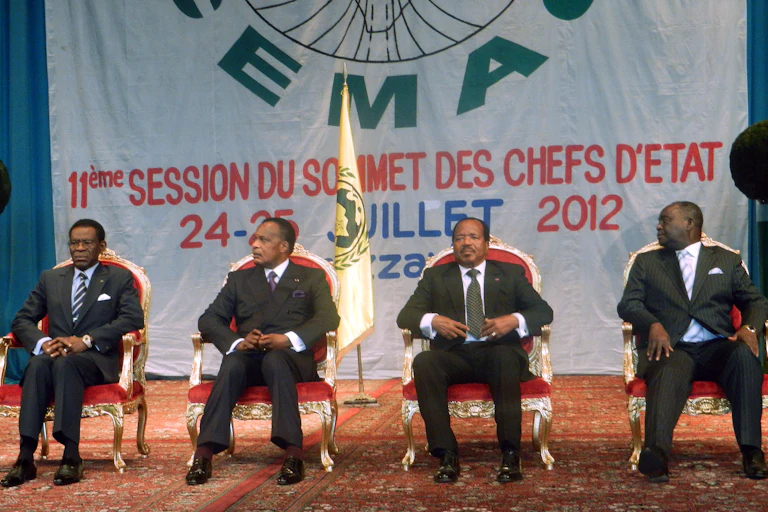 Four men in dark suits, seated in front of a large banner