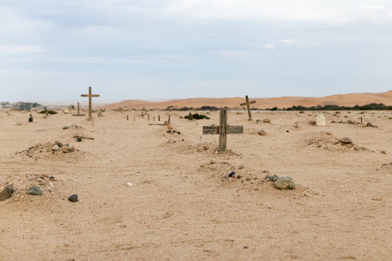 A dusty landscape marked by random, rustic wooden crosses sticking out of the ground.