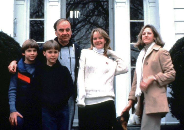 A portrait of the Murdoch family circa 1989: Two teenaged boys with bowl haircuts smile faintly at the camera, a teenaged girl beams, and two middle-aged parents offer wry expressions.