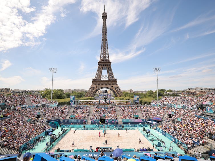 A full stadium of spectators watching a beach volleyball game against the backdrop of the Eiffel Tower.