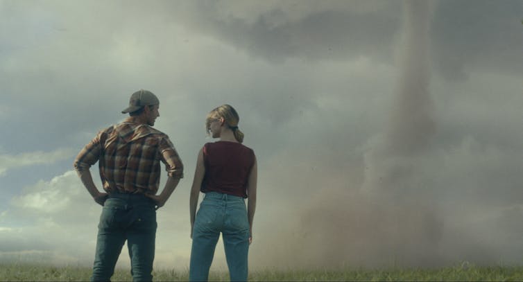 The back of two people seen staring an an ominous sky.
