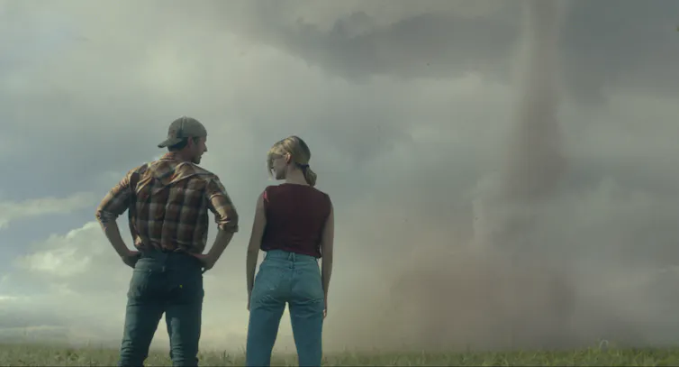 The back of two people seen staring an an ominous sky.