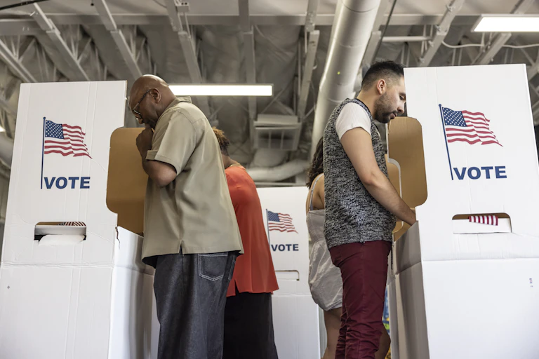 Two men voting at stations that have the US flag on them.