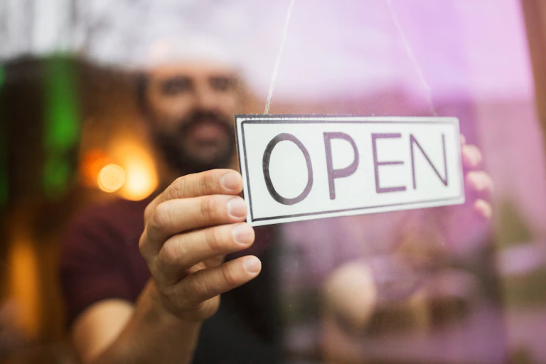 man hanging an Open sign in the window of his premises