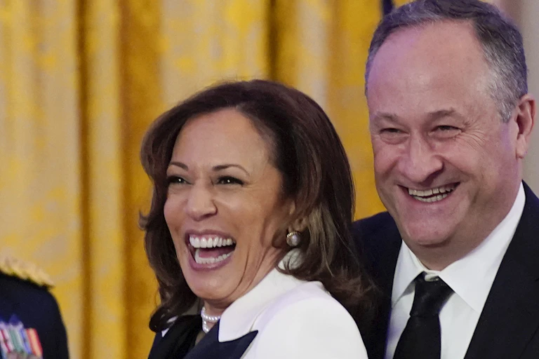 A vice-presidente dos EUA Kamala Harris sorrindo ao lado de seu marido, um homem branco de terno