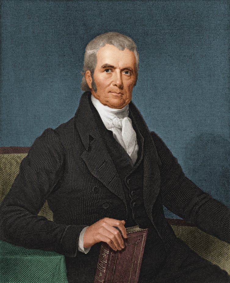 A white man with grey hair and formal clothing sits and holds a brown book in an illustration.