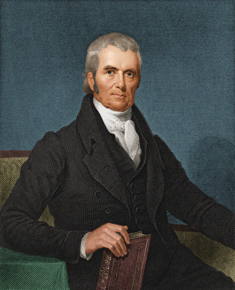 A white man with grey hair and formal clothing sits and holds a brown book in an illustration.