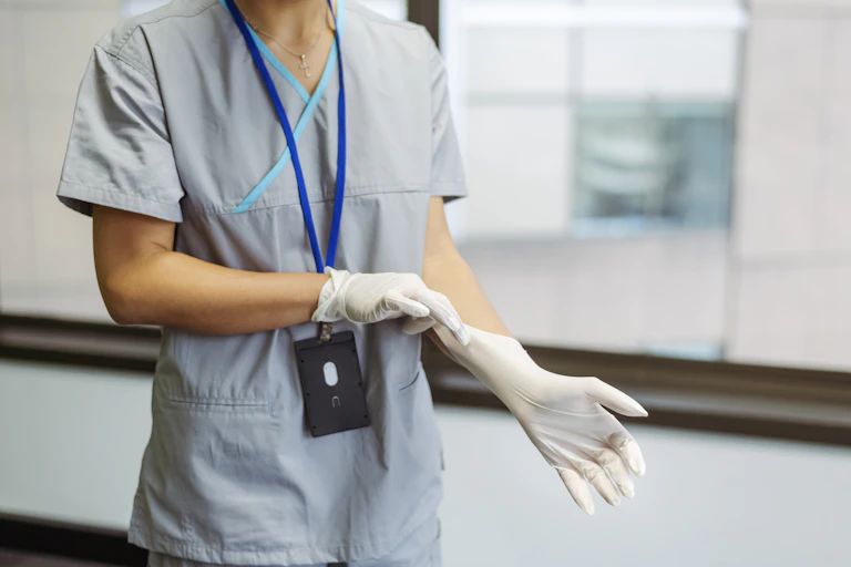 female nurse wearing medical scrubs pulling a surgical glove