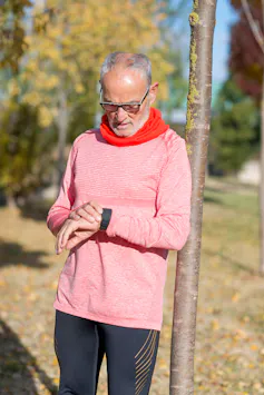 An older man in exercise clothing looks at his smartwatch.
