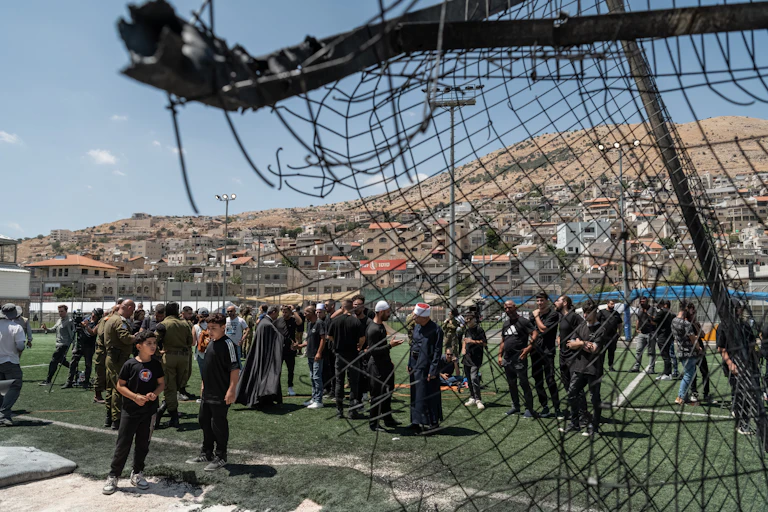 A group of people dressed in black are seen behind a broken fence.
