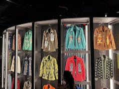 Colourful jackets and shirts in a vintage style hang in rows on an exhibit.