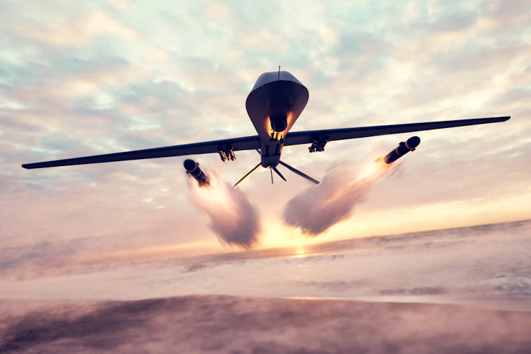 A drone firing two missiles as it flies over a beach.
