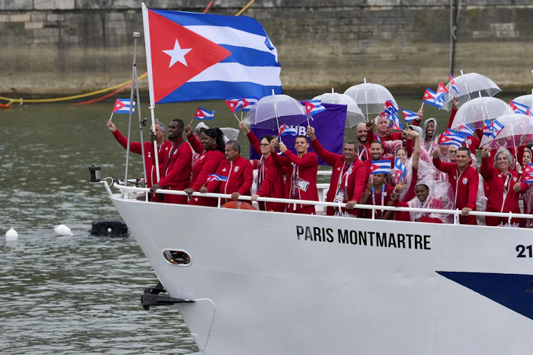 A group of people wearing red tracksuits wave Cuban flags from the prow of a white boat