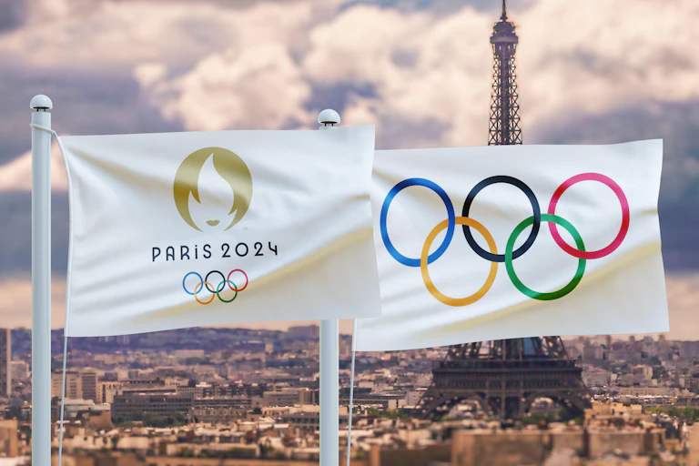The Olympic flag flying against a backdrop of urban Paris and the Eiffel Tower.