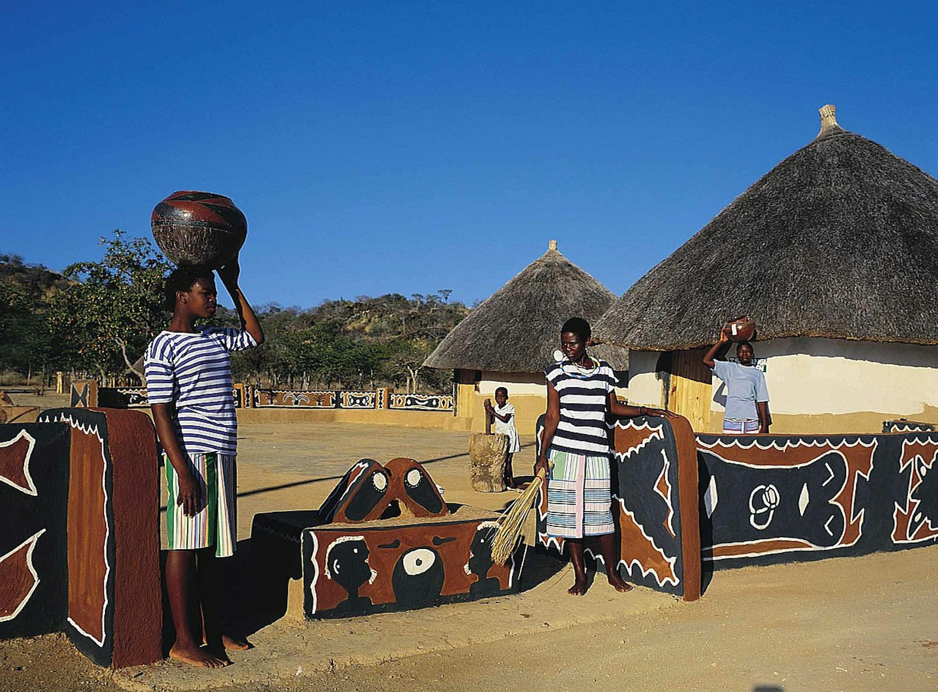 Three people stand in front of houses painted with brown and black designs