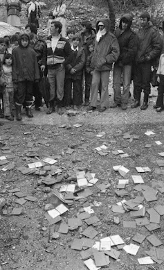 A group of people stands wearing winter clothing. On the ground in front of them are hundreds of Israeli identity cards.