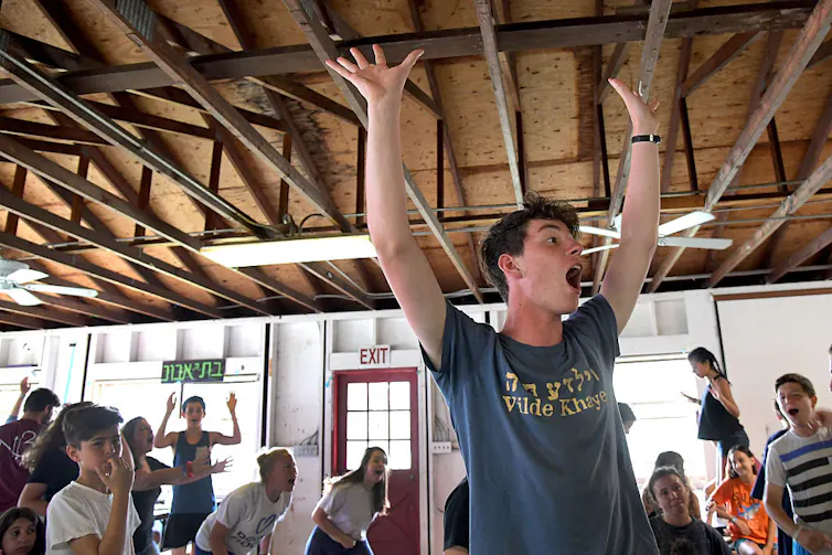 A young man in a blue T-shirt puts his hands in the air as he leads a group of cheering children.