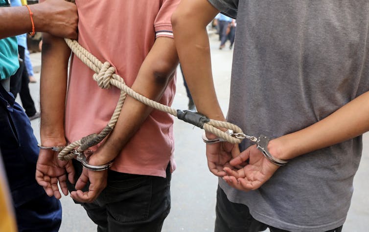 The Bangladeshi police leading away two men in handcuffs.