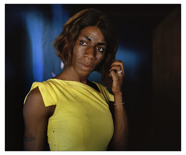 An African woman in a tight-fitting yellow top with a bobbed hairstyle looks pensive.