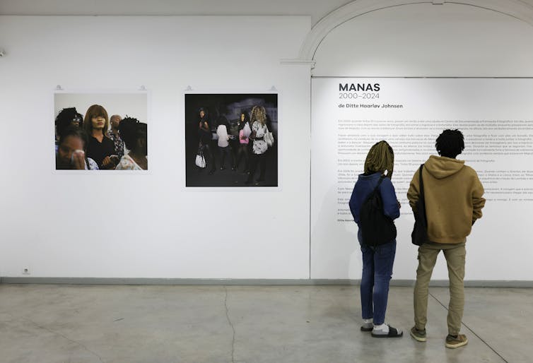 Two people read the information on a wall of a gallery, two photos on display to their left.