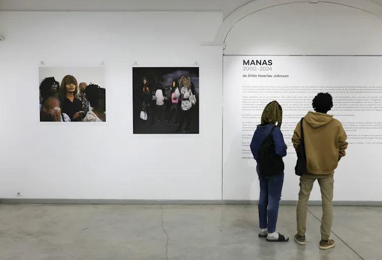 Two people read the information on a wall of a gallery, two photos on display to their left.