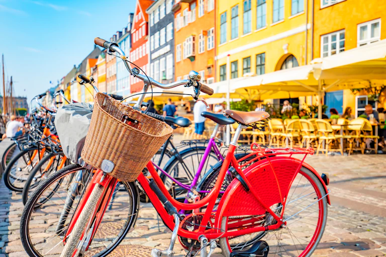 red bike with basket on bike rack, colourful buildings on street behind