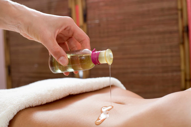 A person pouring oil on a woman's stomach